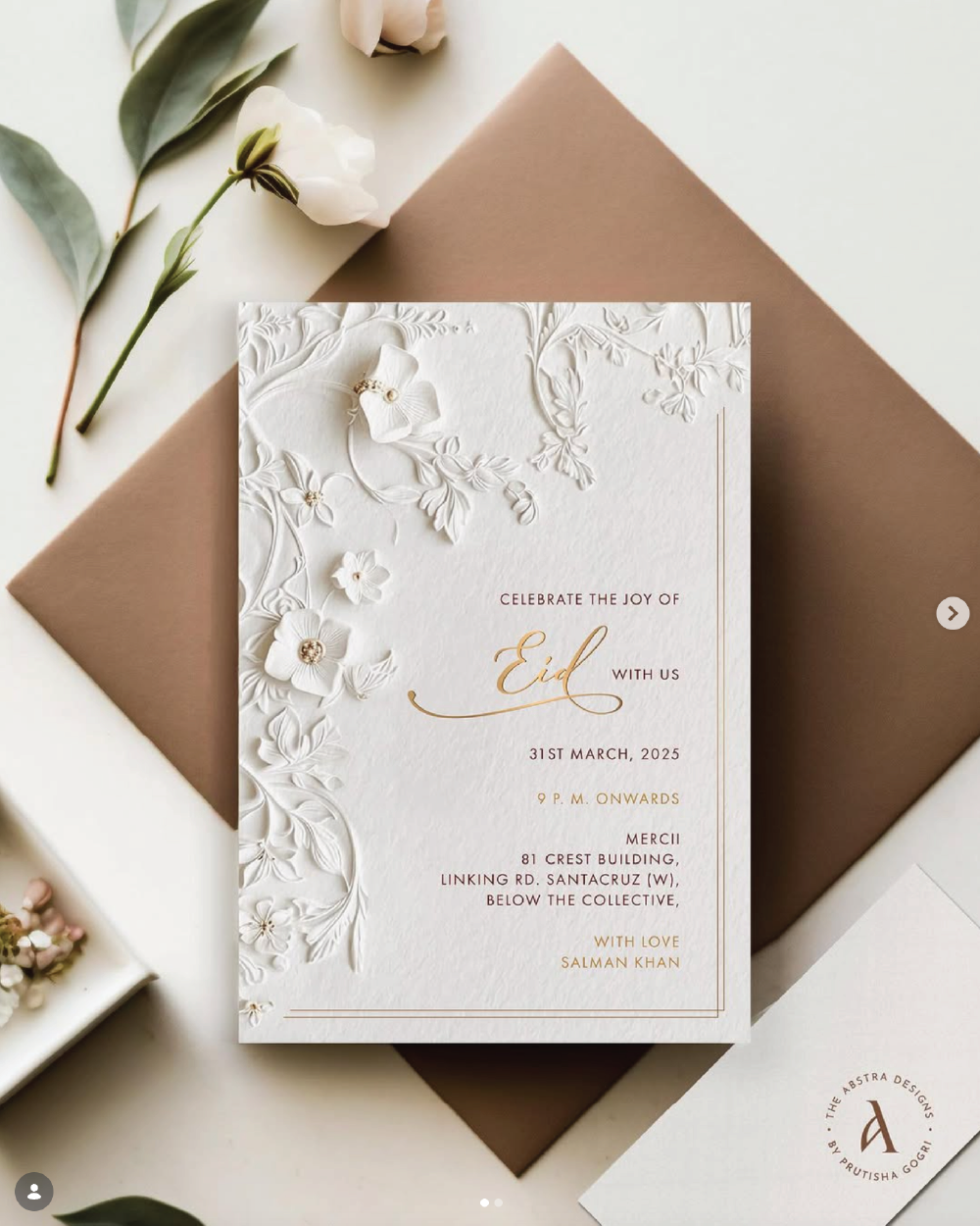 Elegant embossed invitation card with florals and gold lettering on a warm neutral backdrop.