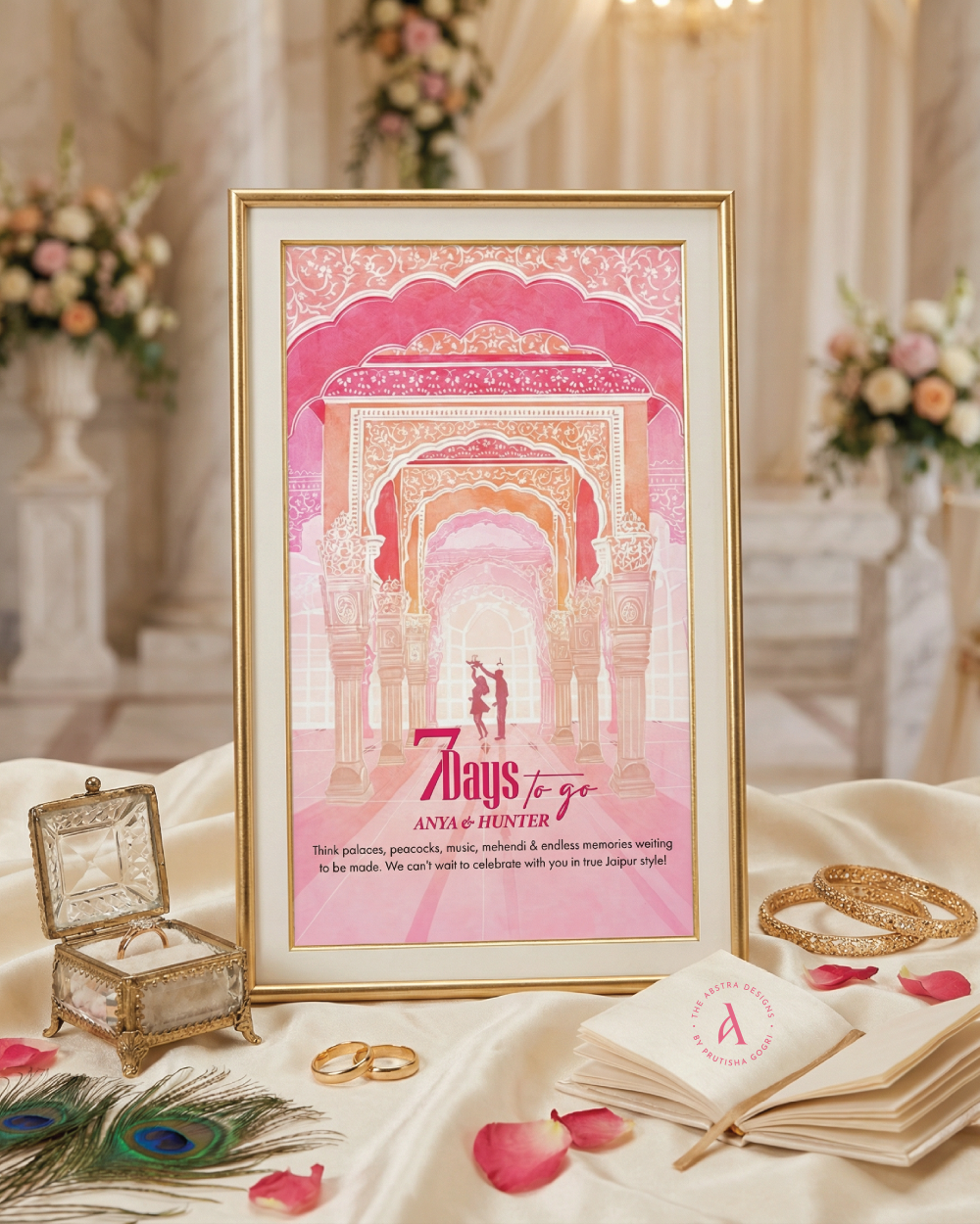 Pink framed wedding countdown sign styled among rings, petals, and peacock feathers.